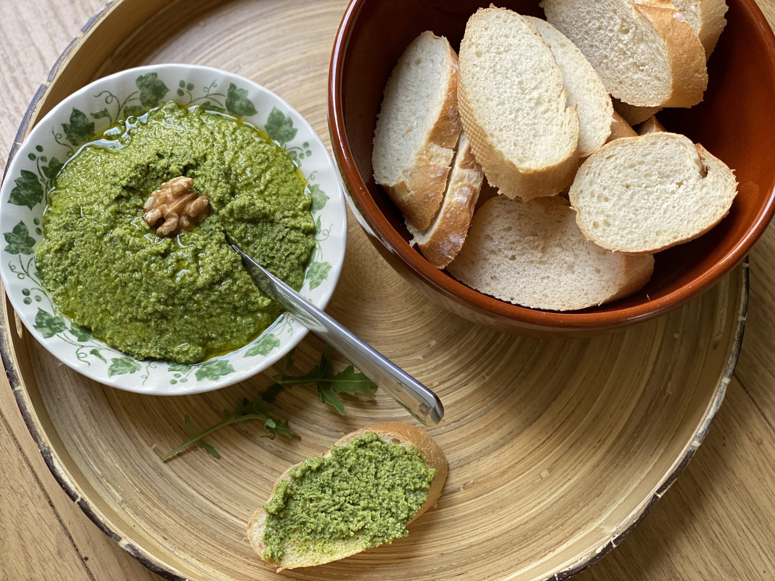 Een schaaltje rucola pesto met een walnoot en een schaal met stokbrood